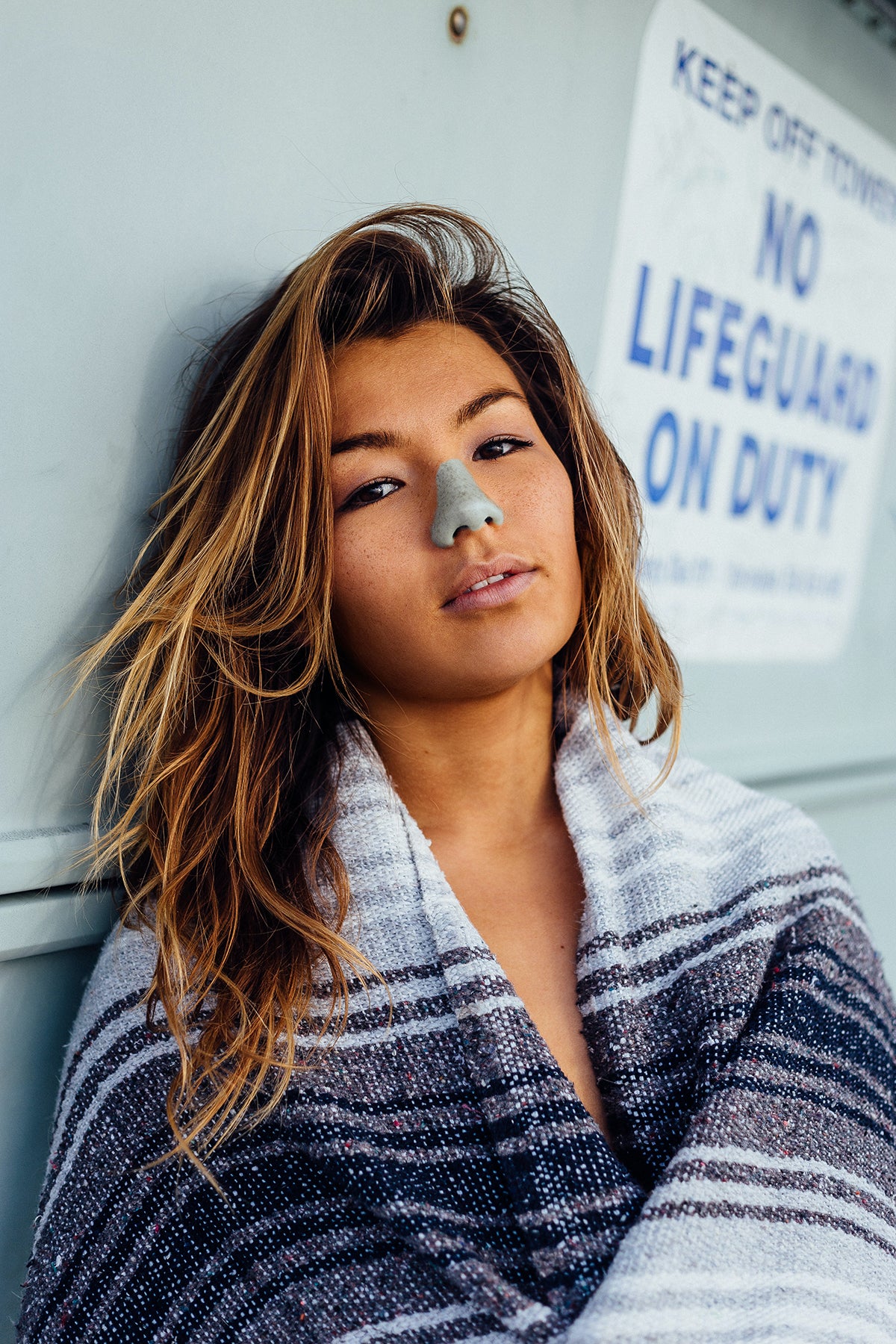 Woman at lifeguard tower protecting her face with the best SPF from Nöz’s reef safe, Zinc oxide, & colorful sunscreen in color blue.